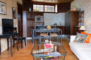 A living room with a glass coffee table, a sofa with a cushion, a TV, a dining area with a table and chairs, a kitchen with cabinets and appliances, and a brick wall. - Indoor heated pool and award-winning vineyard (Arico)
