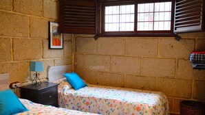Quarto com duas camas, mesa de cabeceira, abajur, janela com persianas, quadro na parede e um cesto.