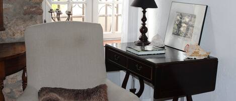 A room with a chair, a desk, a lamp, and a framed picture.