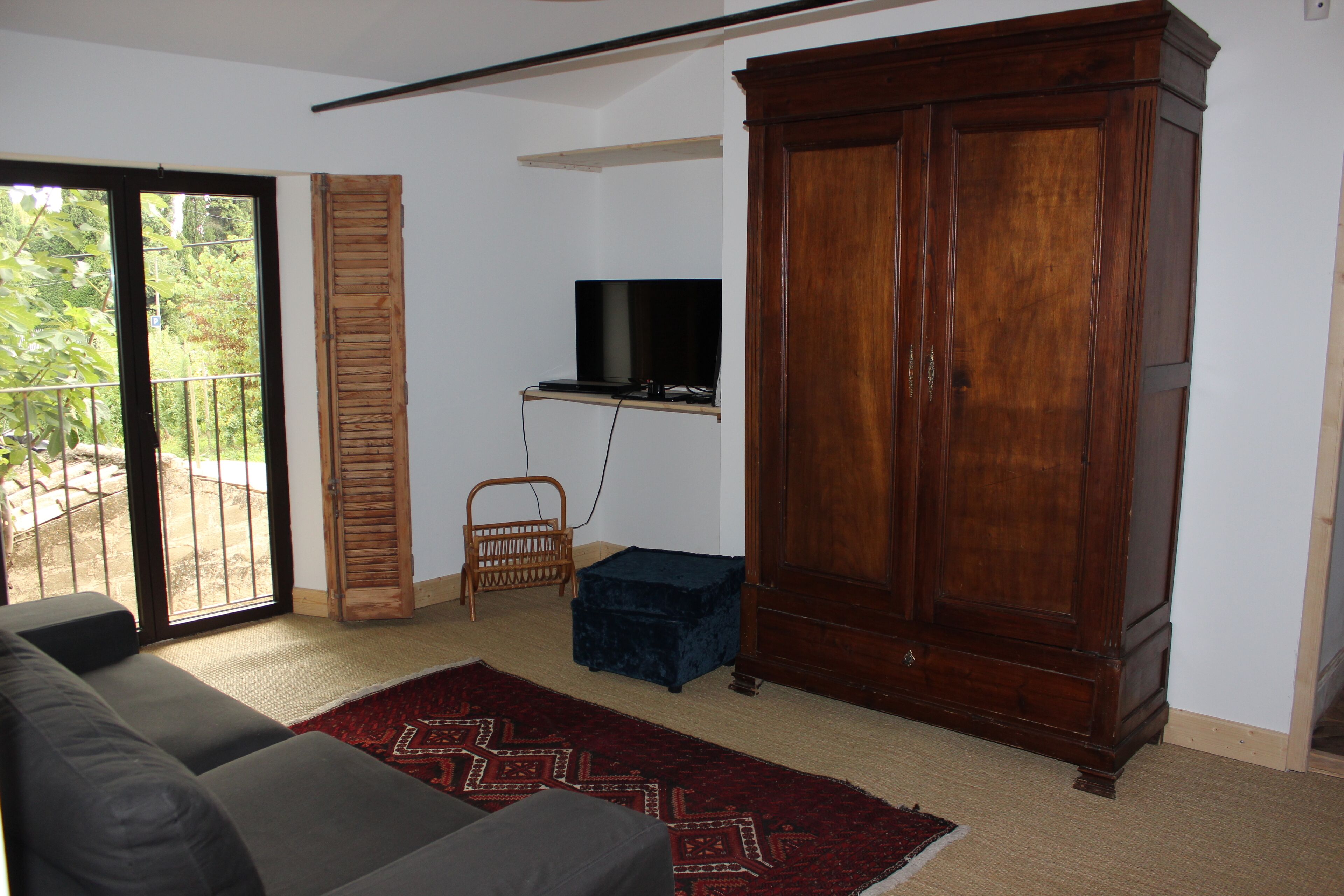 A living room with a sofa, a television mounted on the wall, a wooden cabinet, and a sliding glass door leading to an outdoor area.