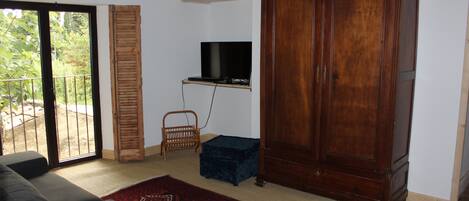 A living room with a sofa, a television mounted on the wall, a wooden cabinet, and a sliding glass door leading to an outdoor area.