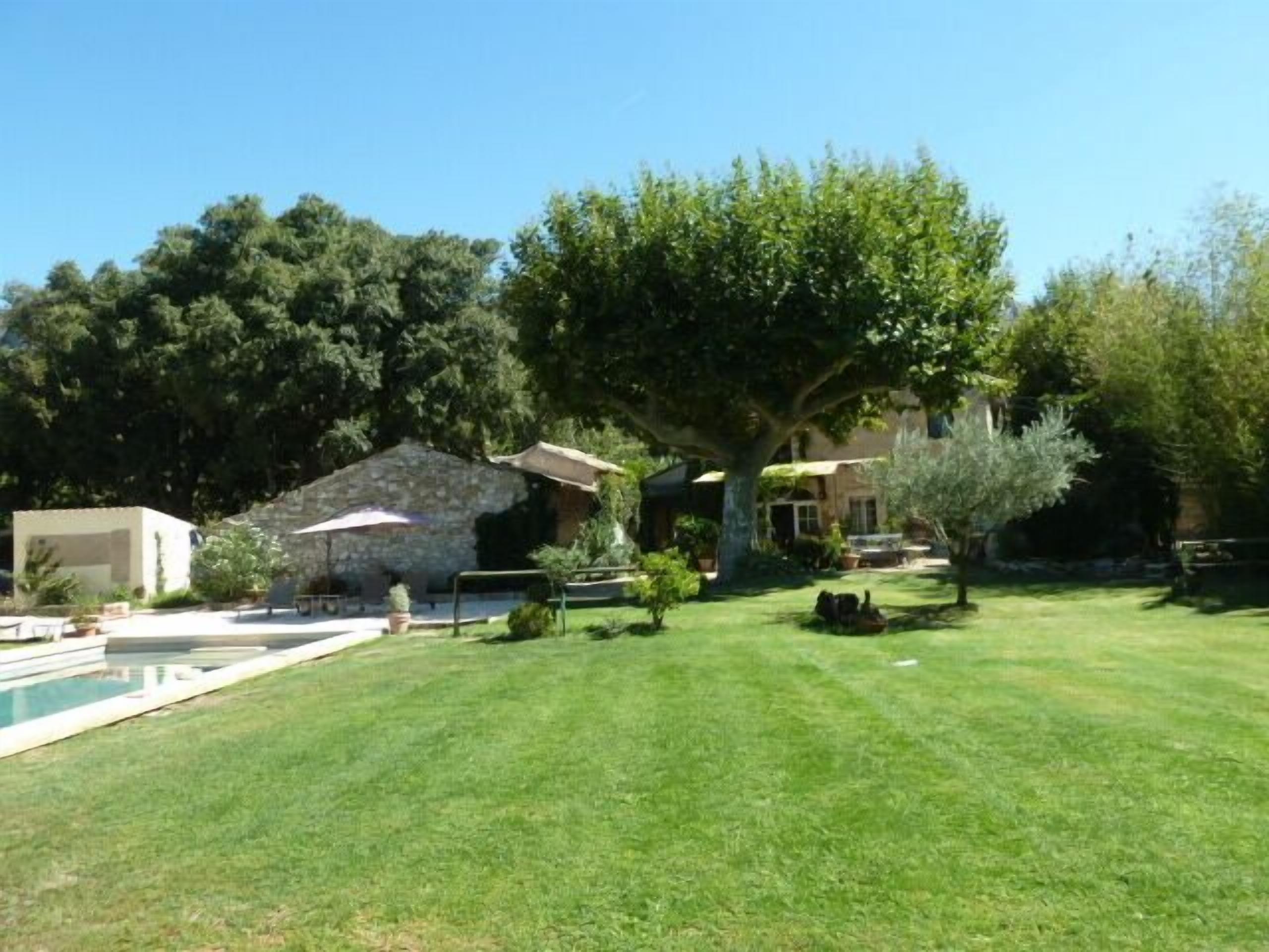 A well-maintained backyard with a swimming pool, a stone building, and a large tree providing shade.