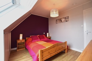 A bedroom with a sloped ceiling, a wooden bed, a nightstand with a lamp, and a wall decoration.