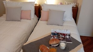 Ein Hotelzimmer mit zwei Betten, jeweils mit weißer und rosa Bettwäsche, einem Nachttisch mit Lampe, einem Tablett mit Croissants, Saft und einer Kerze.