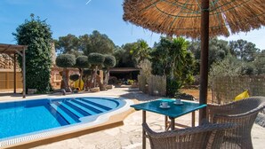 Uma piscina com deck de pedra, móveis de vime e um guarda-sol de palha.