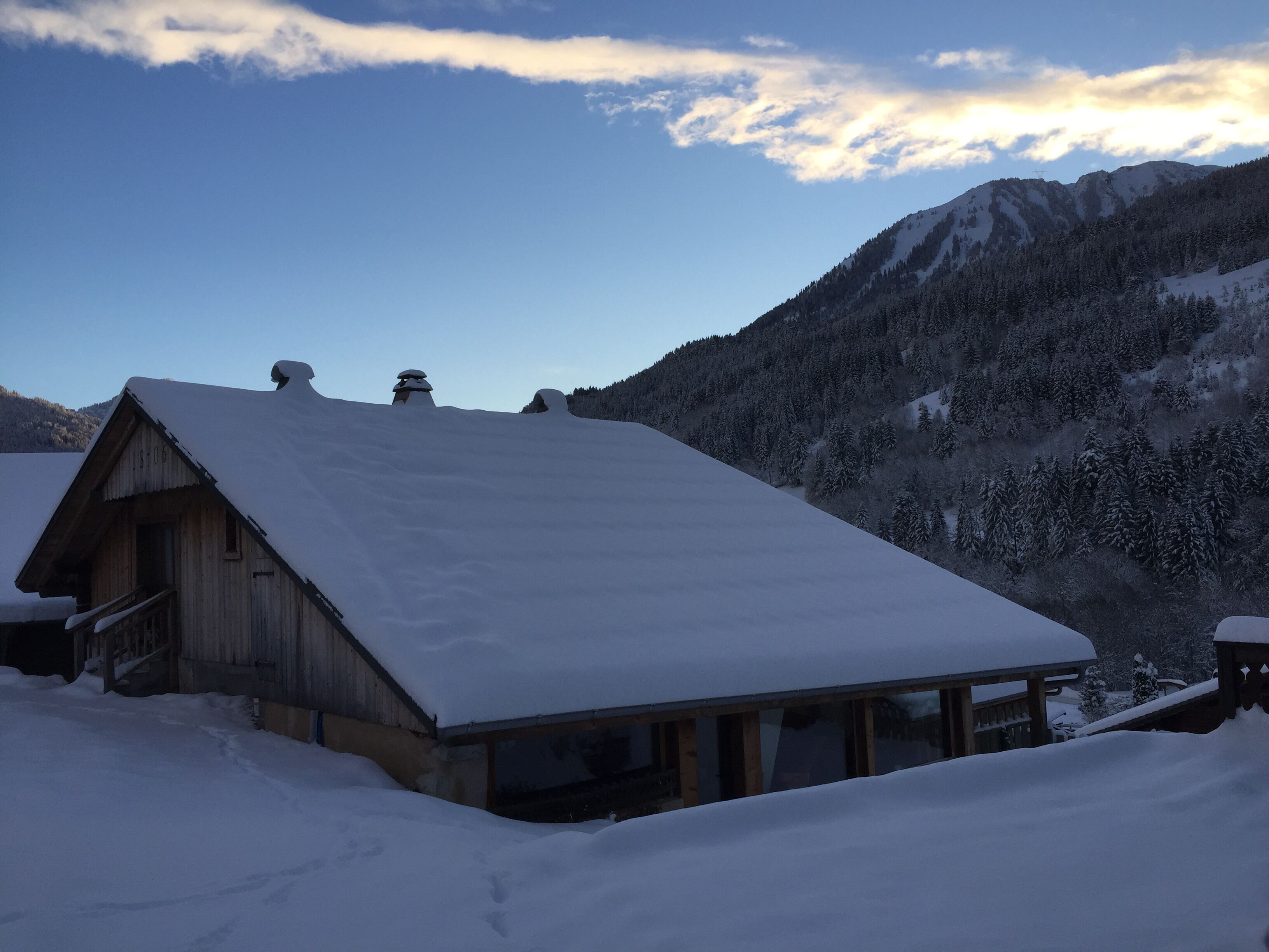 A wooden cabin with a snow-covered roof, surrounded by a snowy landscape and mountains.