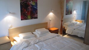 A hotel room with a large bed, a nightstand, a bedside table, a vase with dried plants, and a colorful abstract painting on the wall. - Edge of Nature Reserve; a/c   5* views. Great peace & privacy. Mountains & Sea. (ATRI)