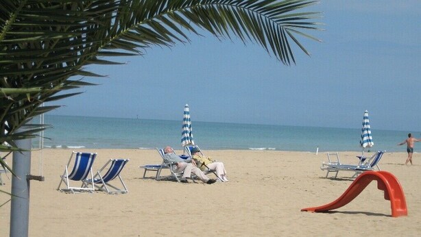 A beach with lounge chairs and umbrellas, a palm tree, and a red slide. - Edge of Nature Reserve; a/c   5* views. Great peace & privacy. Mountains & Sea. (ATRI)