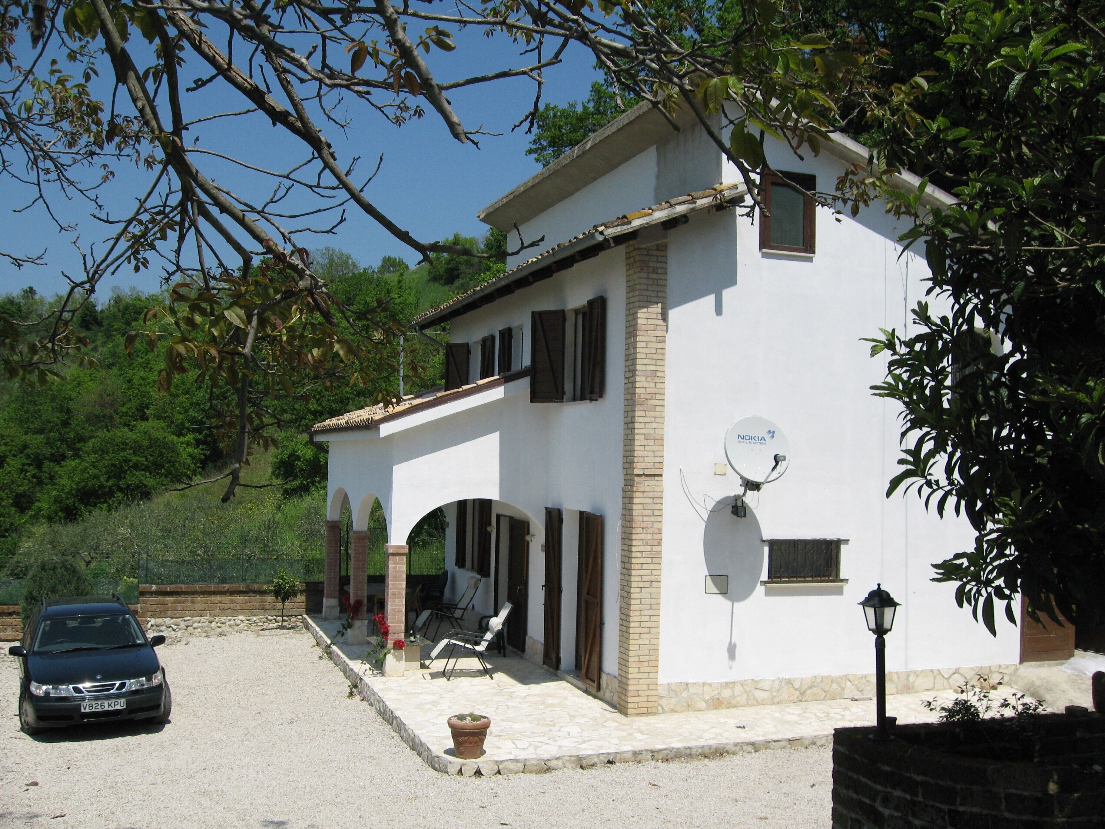 A two-story house with a white exterior, a satellite dish, and a car parked in front.