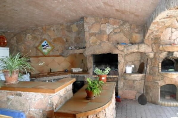 Una habitación con suelo de piedra, chimenea, un banco de piedra y plantas en macetas.