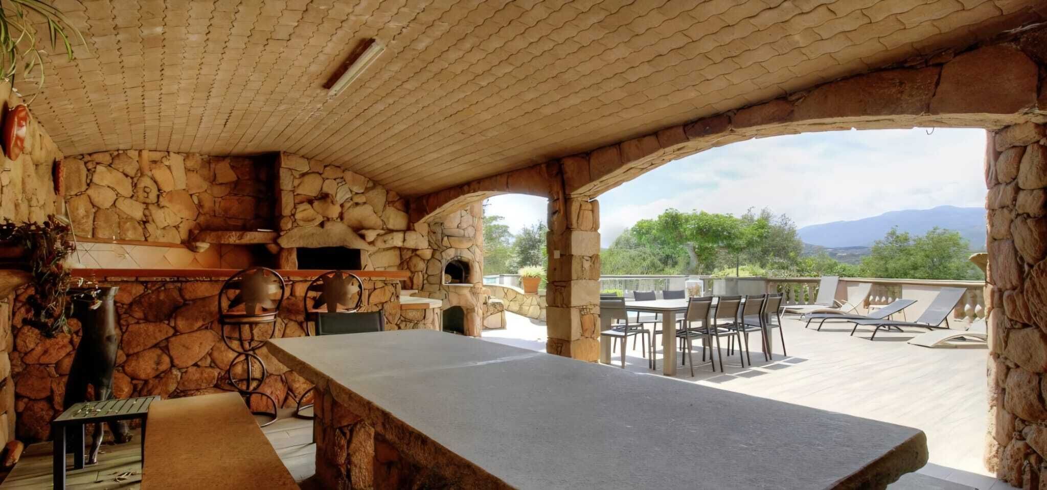 An outdoor patio with a stone fireplace, a dining table, and lounge chairs.