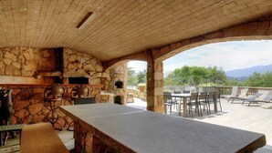 An outdoor patio with a stone fireplace, a dining table, and lounge chairs. - mansion - 8 rooms - 12/13 persons (Porto Vecchio)