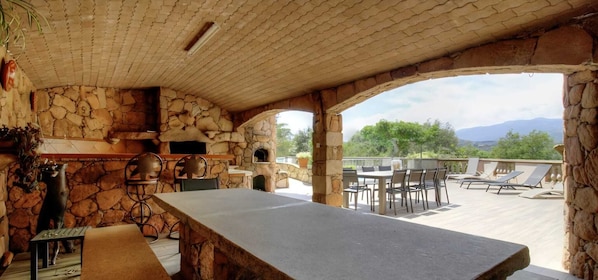 Eine Terrasse im Freien mit Kamin aus Stein, Esstisch und Lounge-Stühlen.