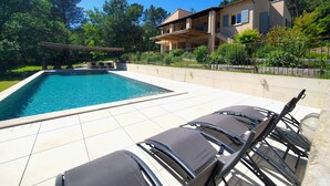 Una piscina con lettini, una zona relax coperta e un edificio con balconi.