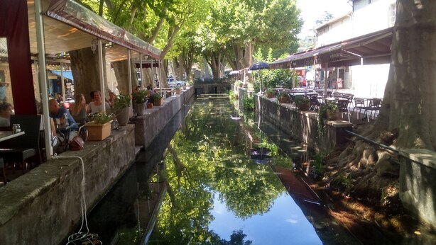 Un ristorante lungo un canale con posti a sedere all'aperto, piante in vaso e vista sull'acqua.