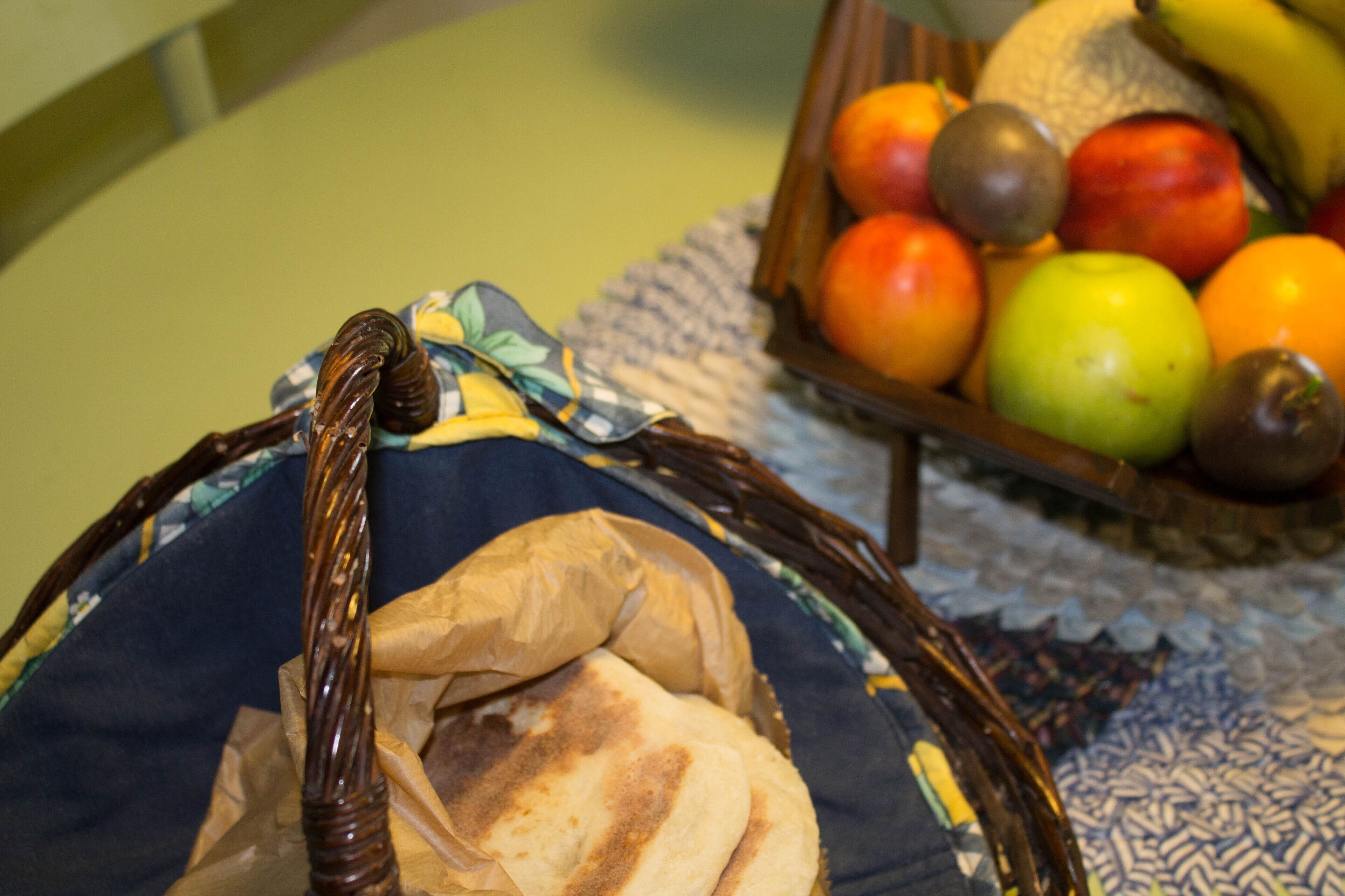 A wicker basket with flatbreads and a bowl of assorted fruits.