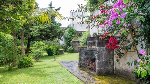 A lush garden with a stone pathway leading to a building with a white facade and a traditional roof. - OLD CHURCH HOUSE  (FURNAS)