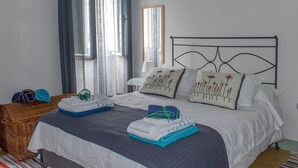 A neatly made bed with a white and gray duvet, two pillows with floral embroidery, and a blue and gray striped blanket. - OLD CHURCH HOUSE  (FURNAS)