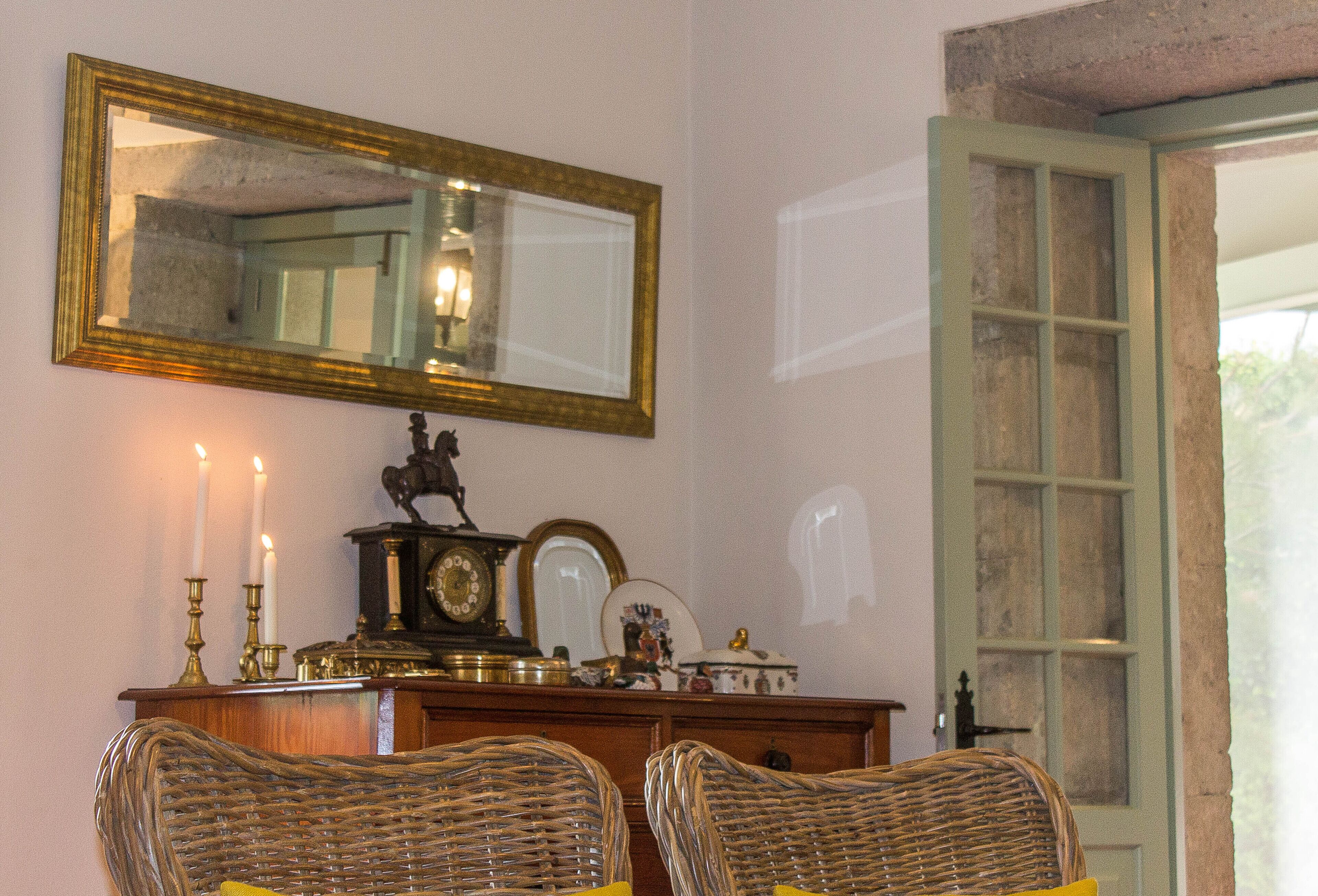 Una habitación con sillas de mimbre, un aparador de madera con espejo, velas y un reloj.