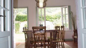 A dining area with a wooden table and chairs, a hanging light fixture, and a view of greenery outside. - OLD CHURCH HOUSE  (FURNAS)