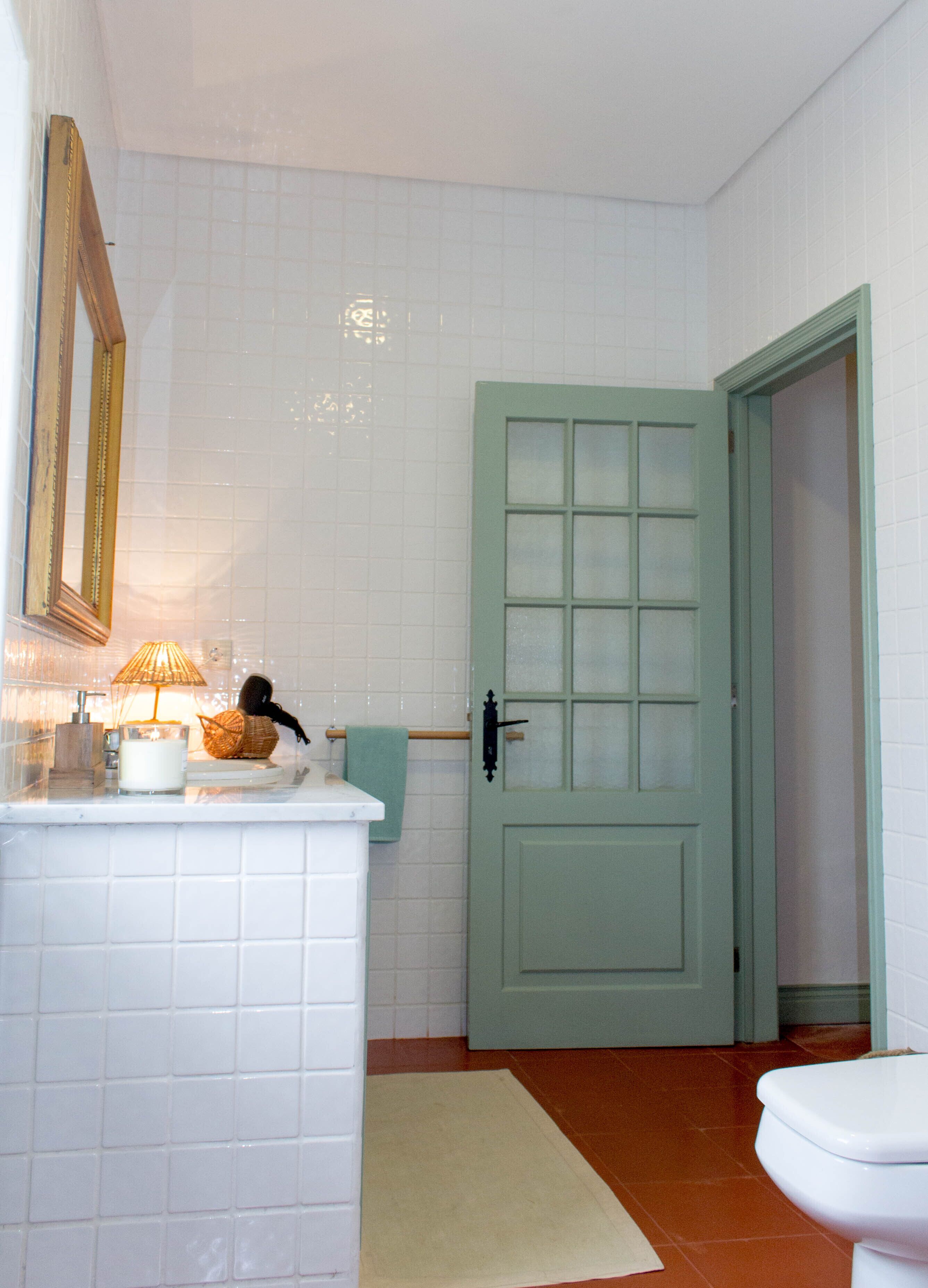A bathroom with white tiled walls, a green door, a white toilet, and a small rug on the floor.
