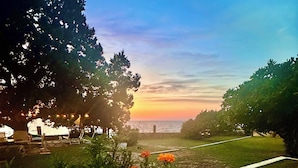 Una vista al atardecer con un sendero que lleva a una masa de agua, rodeado de árboles y flores coloridas.