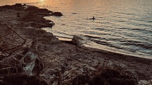 Un paisaje costero con un atardecer sobre el océano, costa rocosa y una persona nadando.