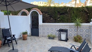 A patio with a tiled floor, a black umbrella, two lounge chairs, a potted plant, and a metal grill. - 4 Bedroom Townhouse With Pool Close To Town, Beach And Park - Free WiFi (Benalmadena Cost)