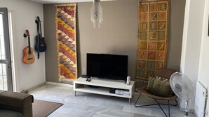 A living room with a TV, two guitars, a patterned rug, a fan, and a couch. - 4 Bedroom Townhouse With Pool Close To Town, Beach And Park - Free WiFi (Benalmadena Cost)