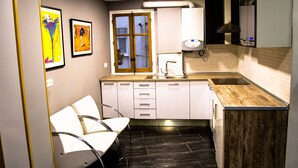 Una cocina moderna con armarios blancos, encimera de madera, horno empotrado y ventana con vistas. En la zona contigua hay dos sillas blancas y una mesita.