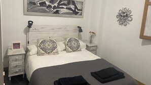 Un dormitorio ordenado con una cama, dos mesitas de noche, un tocador, una obra de arte en la pared y un adorno decorativo.