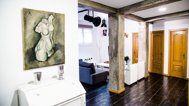 Un interior moderno con suelo de madera oscura, una pared blanca con un cuadro, un sofá azul y puertas de madera.