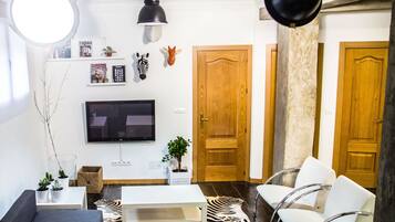 Una sala de estar moderna con una televisión de pantalla plana, un sofá, una mesa de centro y dos sillones. Hay adornos en la pared y un tapete con estampado de cebra en el suelo.