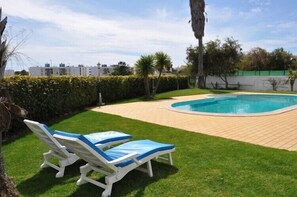 Une piscine avec deux chaises longues et une pelouse bien entretenue.