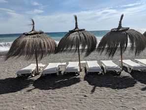 Ein Strand mit Strohdächern und weißen Liegestühlen, die in Reihen angeordnet sind.