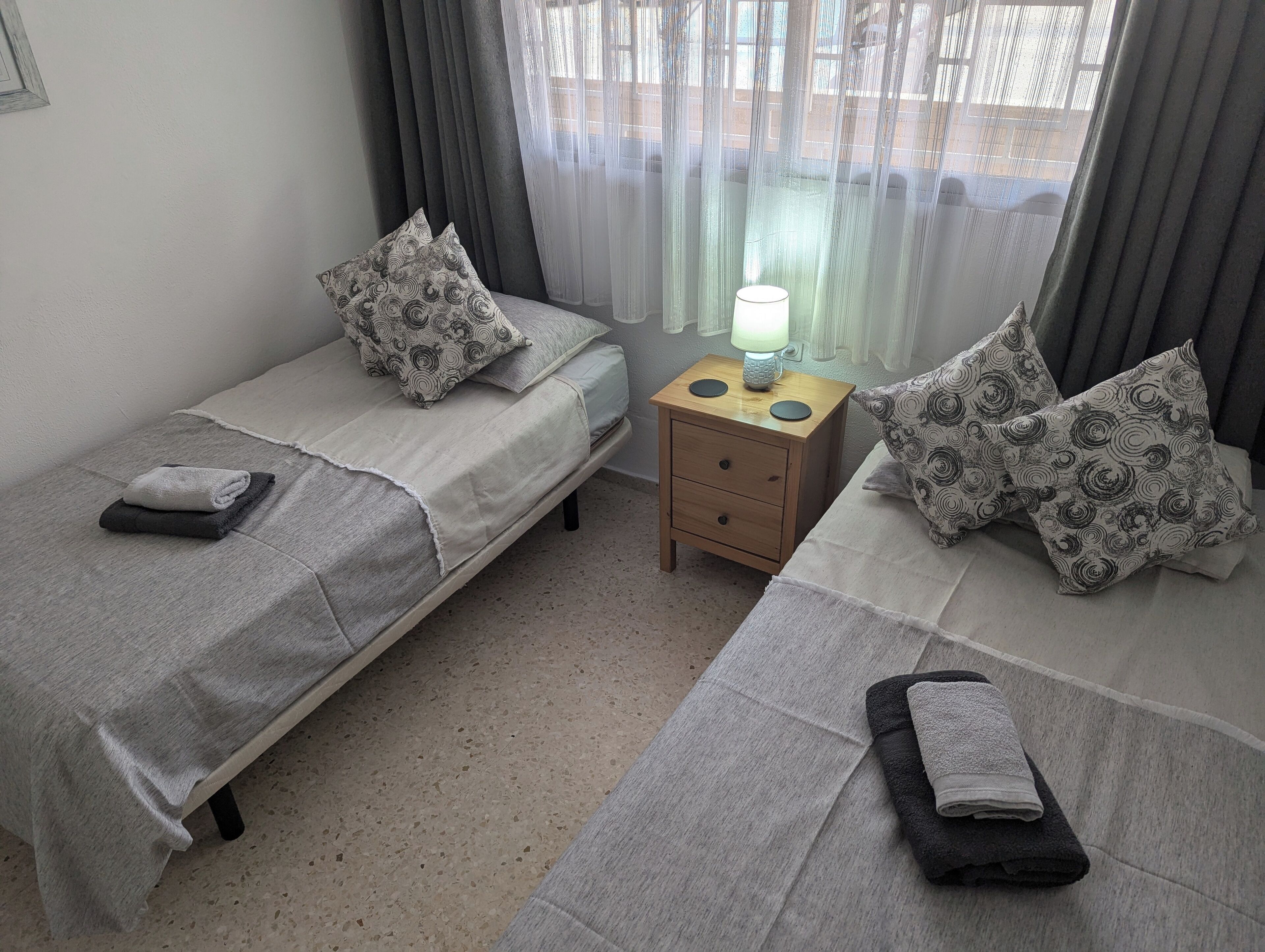 Ein Zweibettzimmer mit zwei Betten, jedes mit gemusterten Kissen und einem Nachttisch mit Lampe.