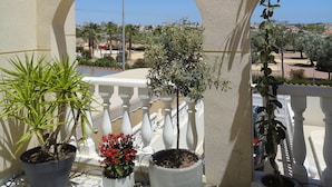 Un balcón con plantas en macetas, baranda blanca y vista a una zona residencial.