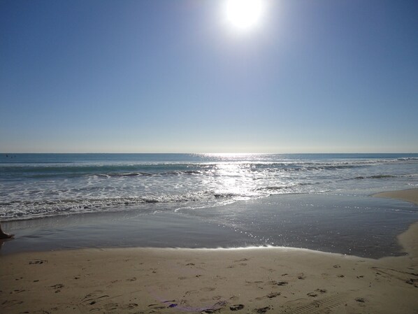 Ein Strand mit blauem Himmel und Sonnenschein, der sich im Wasser spiegelt.