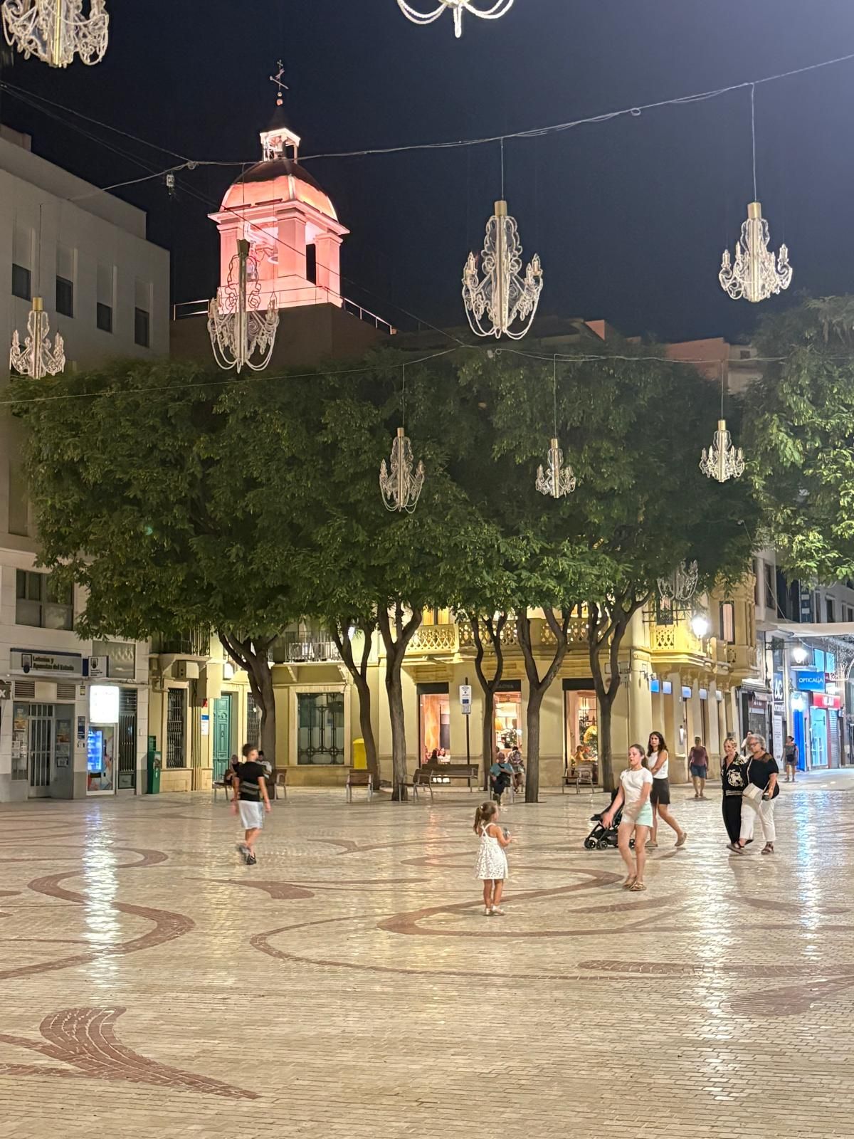 An open plaza with a tiled floor, trees, and hanging chandeliers.