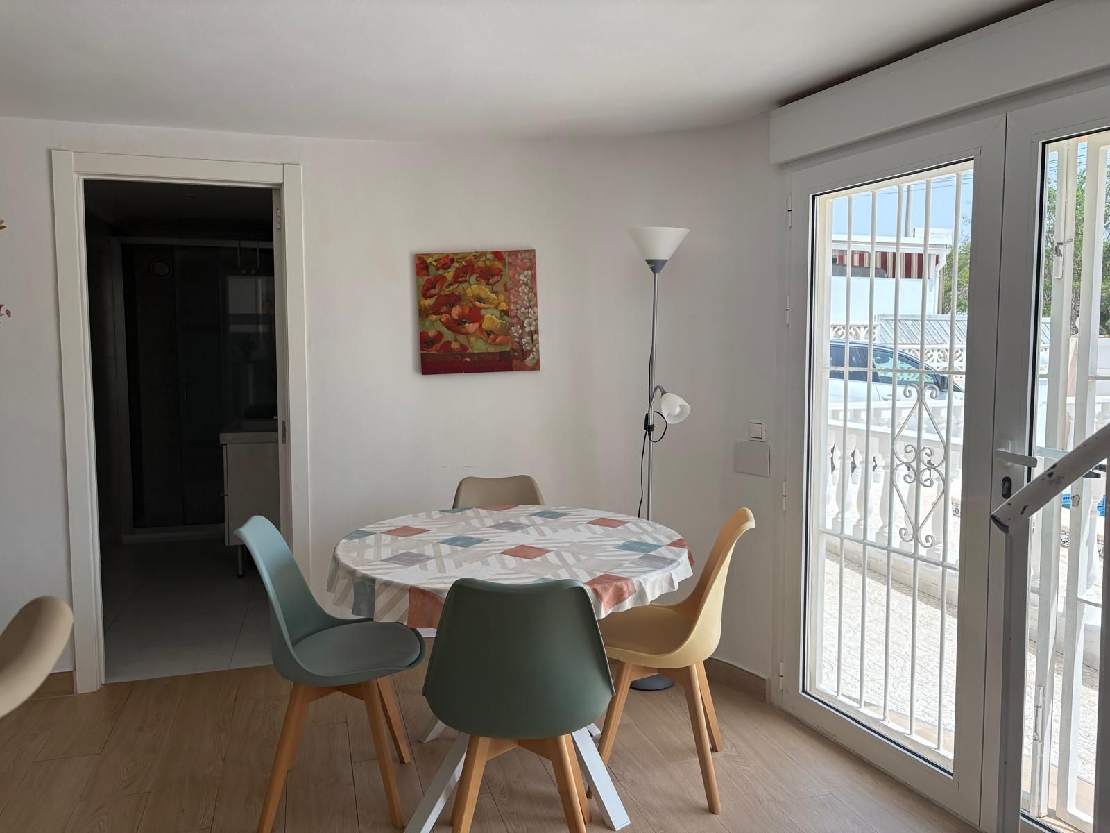 A dining area with a round table, four chairs, a floor lamp, and a door leading to an outdoor balcony.