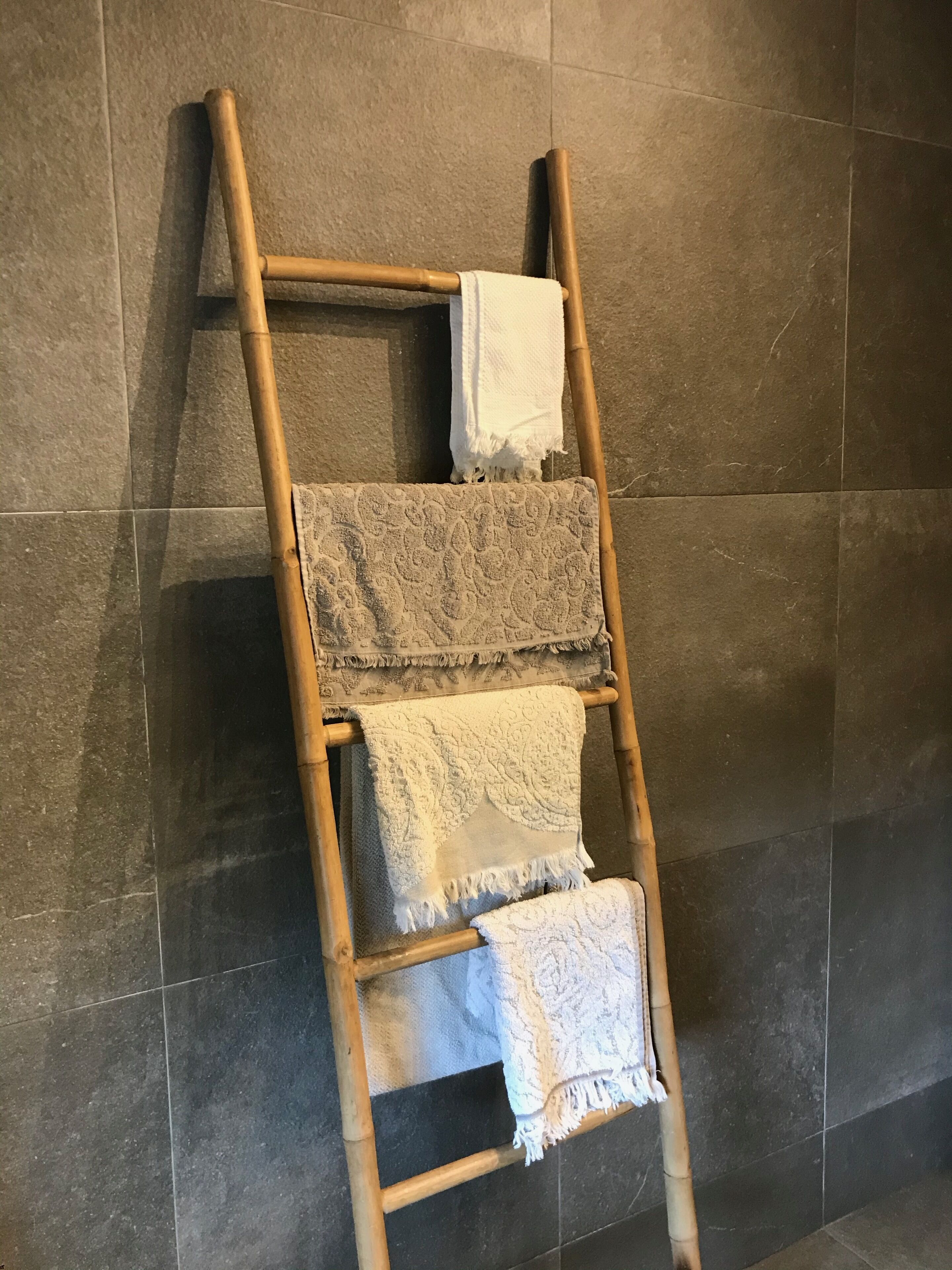 Um porta-toalhas de madeira com três toalhas penduradas em uma parede revestida de azulejos.