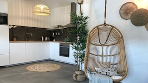 Una cucina moderna con mobili bianchi, forno integrato e una sedia in rattan sospesa.