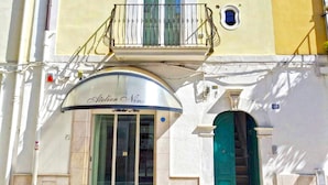Ein Gebäude mit einem Laden im Erdgeschoss namens „Atelier Nino“, einem Balkon mit Metallgitter und einer grünen Tür.