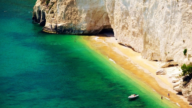 Eine Küstenlandschaft mit klarem türkisblauem Wasser, einem Sandstrand und felsigen Klippen.