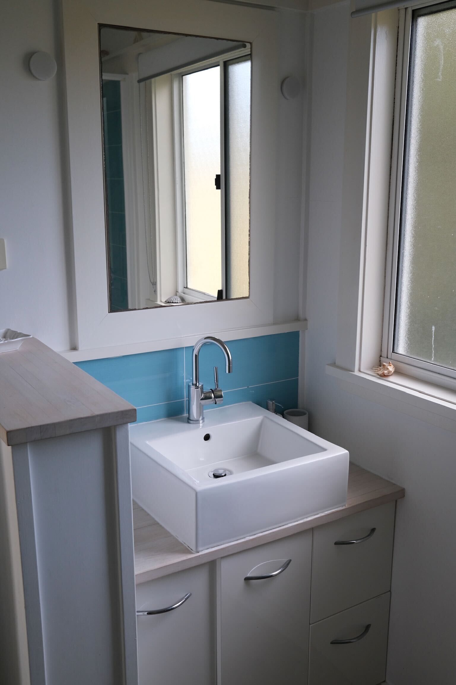 Un baño con lavamanos blanco, un espejo y una ventana.