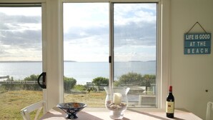 Une table à manger avec un saladier, un verre avec une bougie et une bouteille de vin, donnant sur une plage où est affiché un panneau indiquant : « LA VIE EST BELLE À LA PLAGE ».