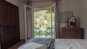 Un dormitorio con cama, cómoda, espejo y vista a un patio exterior con sillas y una mesa.