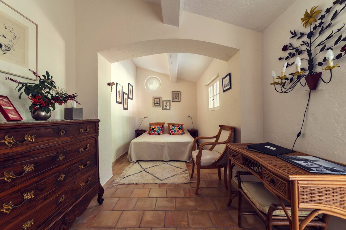 A bedroom with a bed, dresser, chair, and a desk with a lamp.