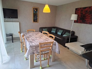 Un salon comprenant une table à manger, des chaises, un canapé, un téléviseur et une lampe.
