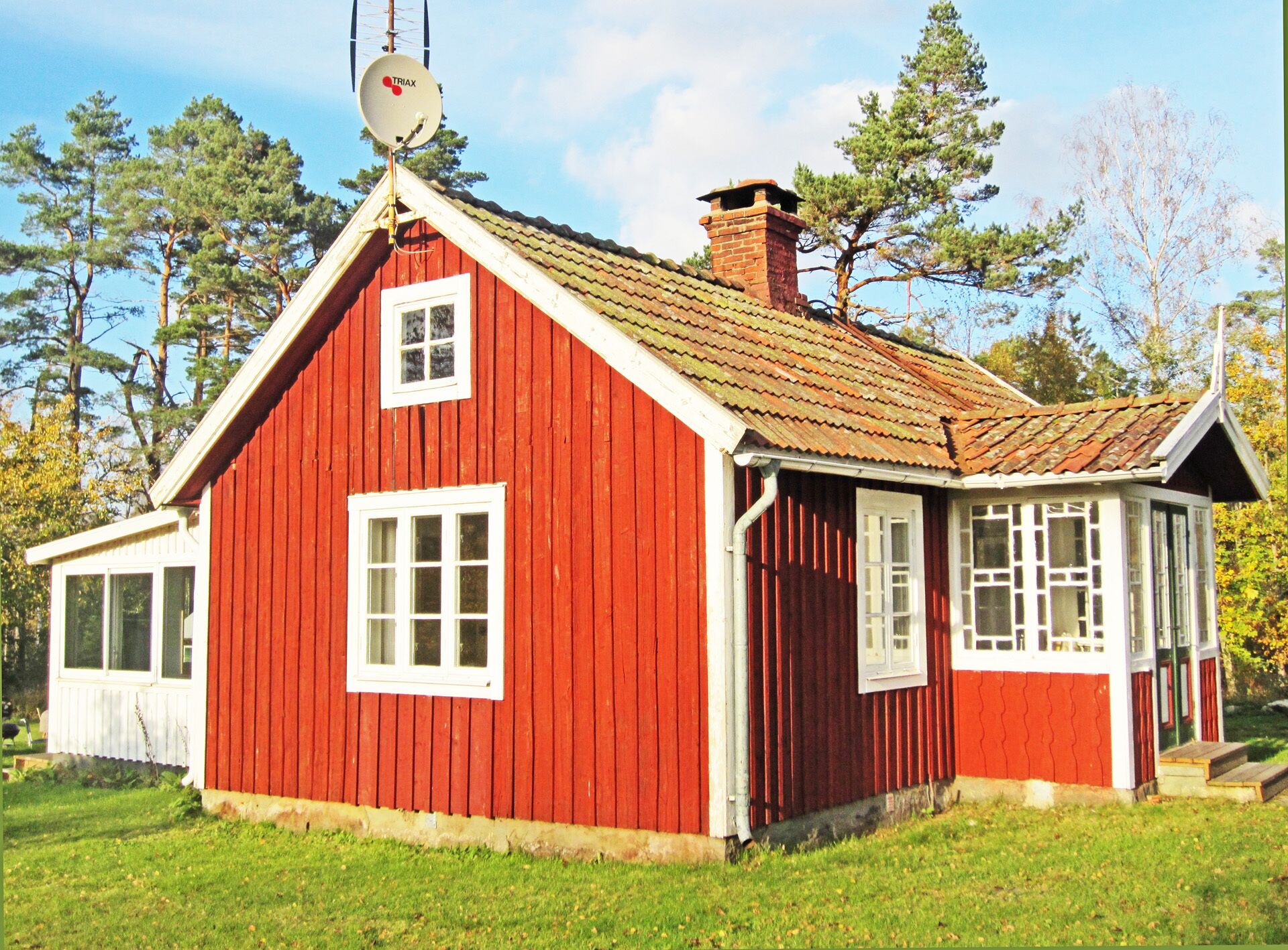 A red wooden house with a tiled roof, a chimney, and a satellite dish.